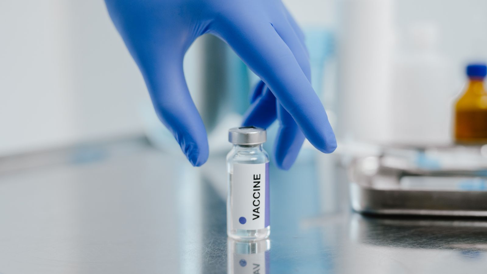 A gloved hand holds a small glass vial upright on a metal laboratory surface.